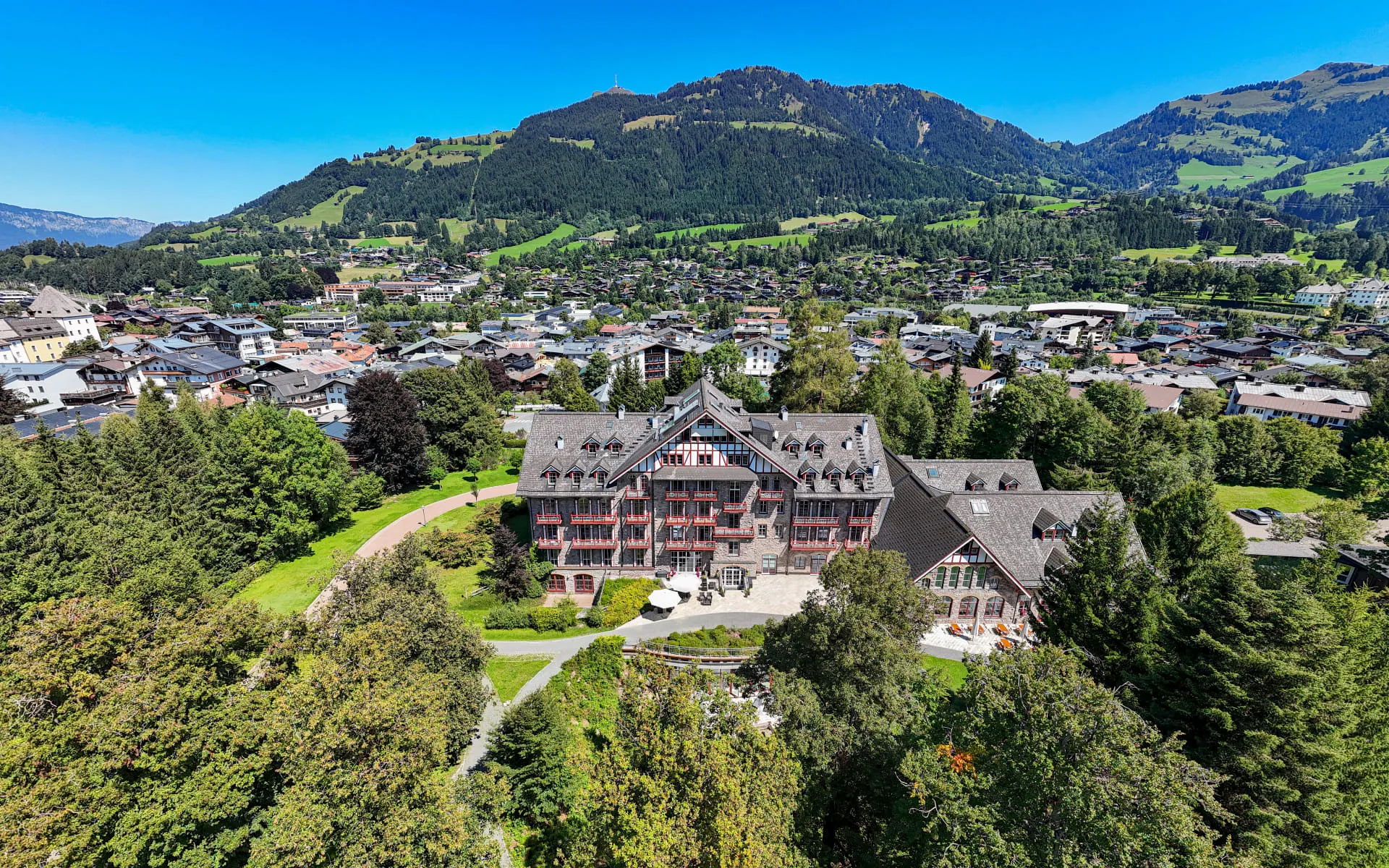 Aerial view of Grandhotel surrounded by trees and mountains, overlooking a town.